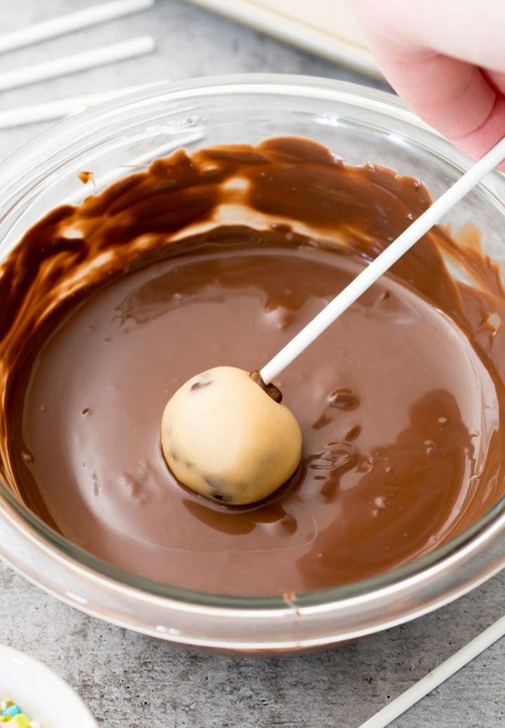 Cookie dough pop being rolled in melted chocolate