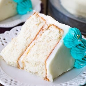 Slice of white cake with white icing and blue icing decorations on plate