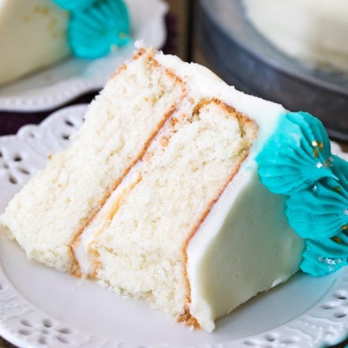 Slice of white cake with white icing and blue icing decorations on plate