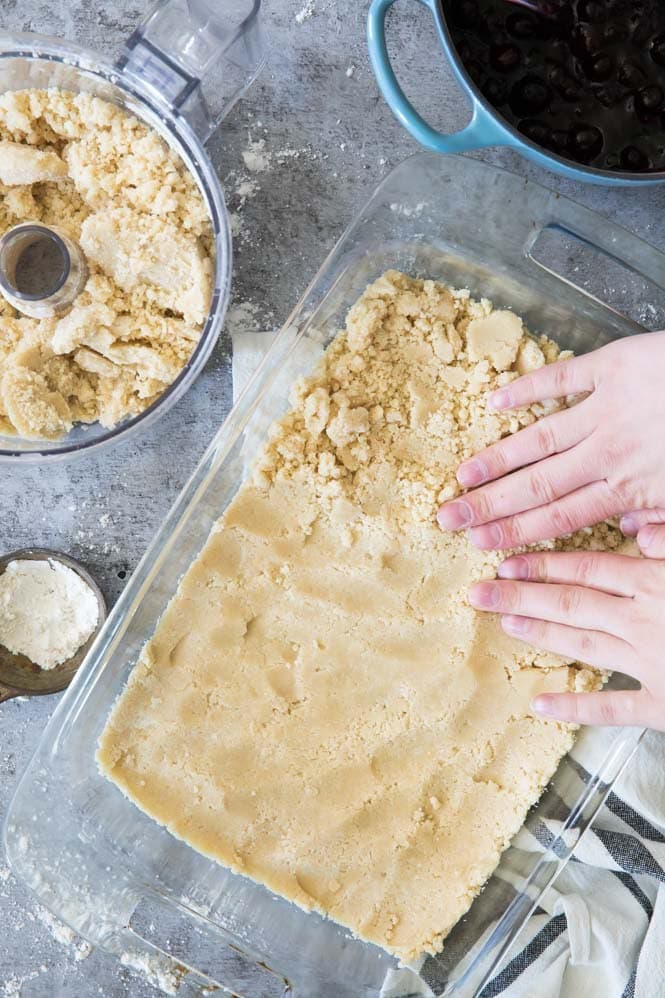 Pressing shortbread crumble into the bottom of a pan for blueberry crumb bars