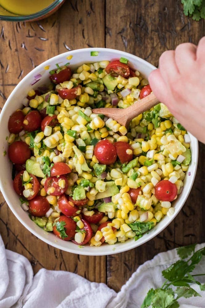 corn salad being stirred by hand in white bowl