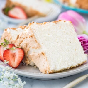 Two slices of angel food cake on a white plate next to strawberries