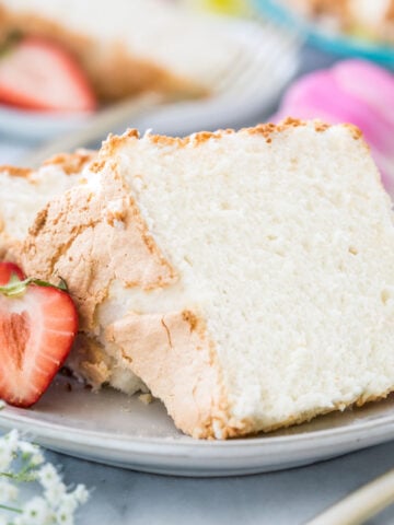 Two slices of angel food cake on a white plate next to strawberries