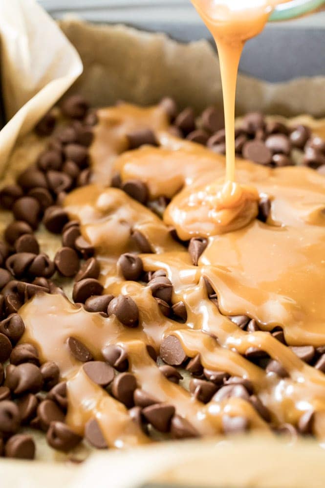 Pouring melted caramel over chocolate chips for carmelitas
