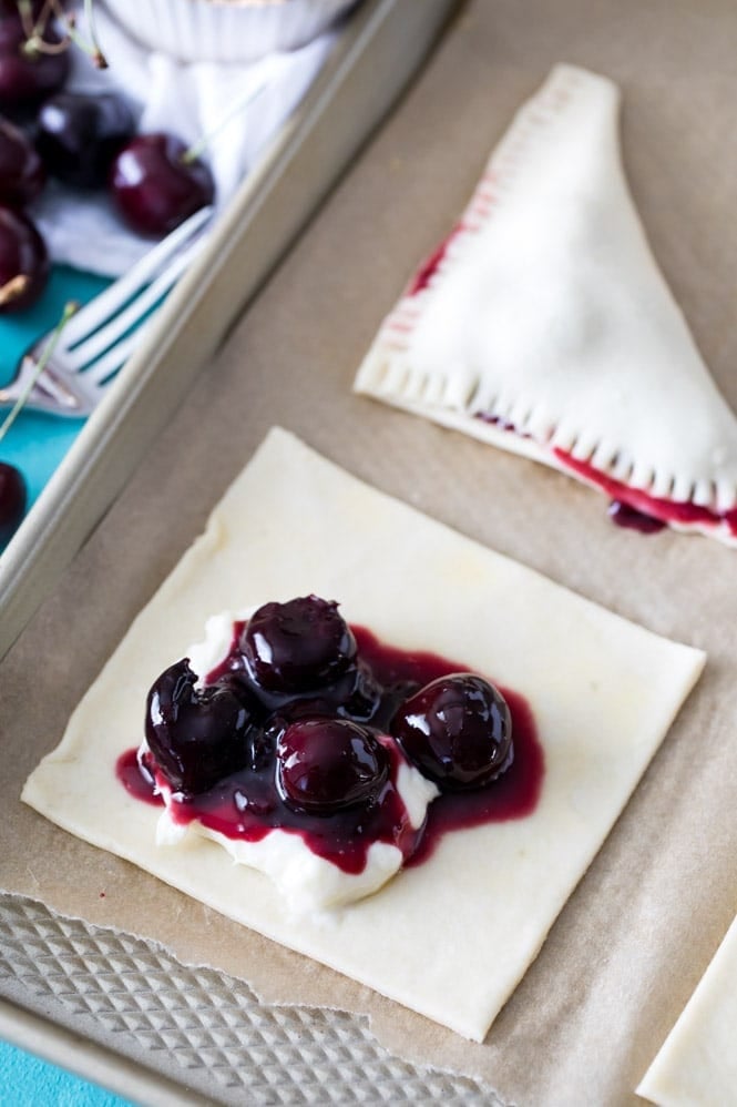 Filling a square of pie dough with cheesecake and cherry filling