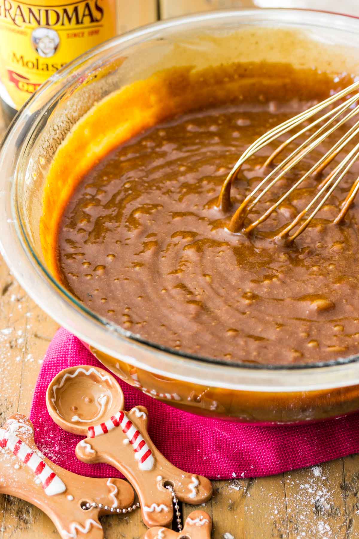 Gingerbread batter being whisked in a glass bowl with two gingerbread cookie shaped measuring spoons inforeground