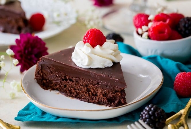 Slice of flourless chocolate cake on plate topped with berries and cream