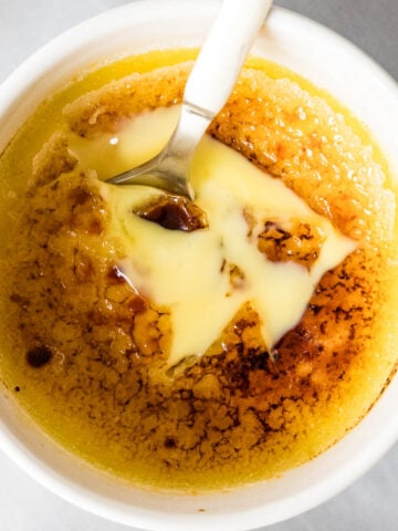 Overhead of creme brulee in a ramekin - golden spoon broke through surface to show custard beneath