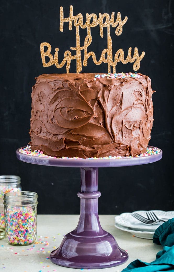Chocolate frosted birthday cake on a purple cake stand