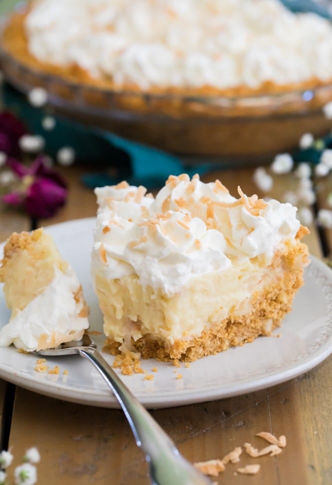 Slice of coconut cream pie with bite out of it on white plate