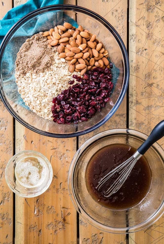 Ingredients for making homemade granola: dry ingredients in large bowl, wet ingredients in smaller bowl, egg white in smallest bowl.