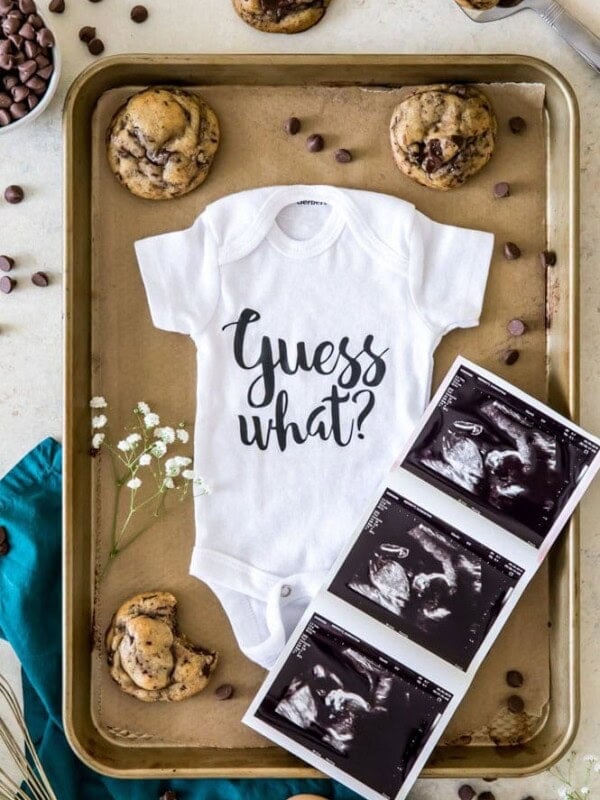 Baby onesie with ultrasound pictures surrounded by cookies and chocolate