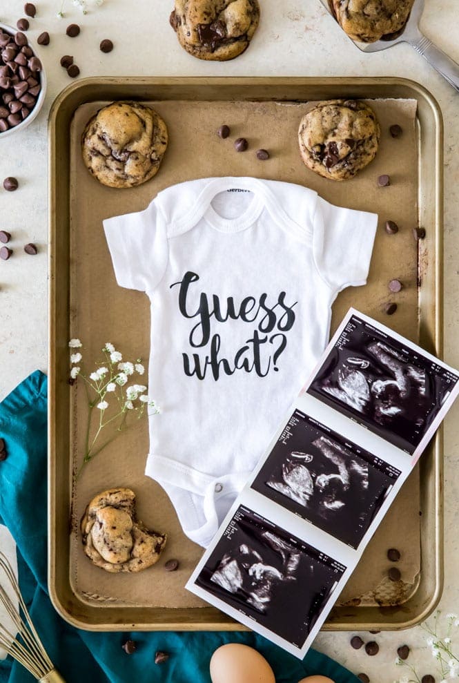 Baby onesie with ultrasound pictures surrounded by cookies and chocolate