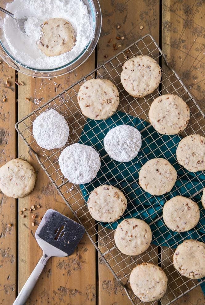 Pecan sandies on cooling rack, some being tossed in powdered sugar