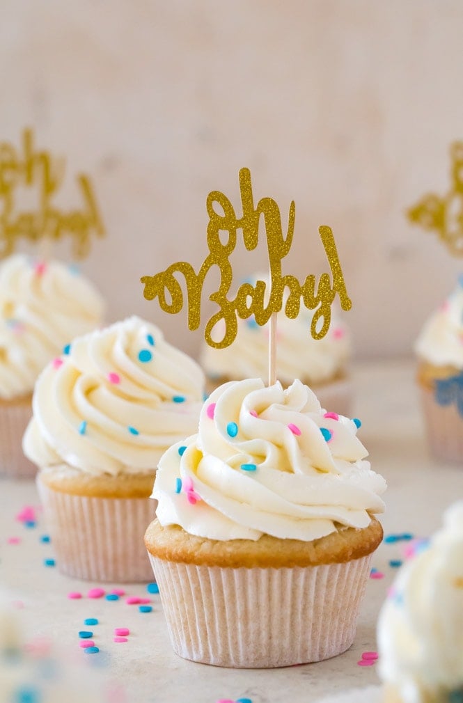 Vanilla cupcake with white icing and blue and pink sprinkles and gold "oh baby" cupcake topper