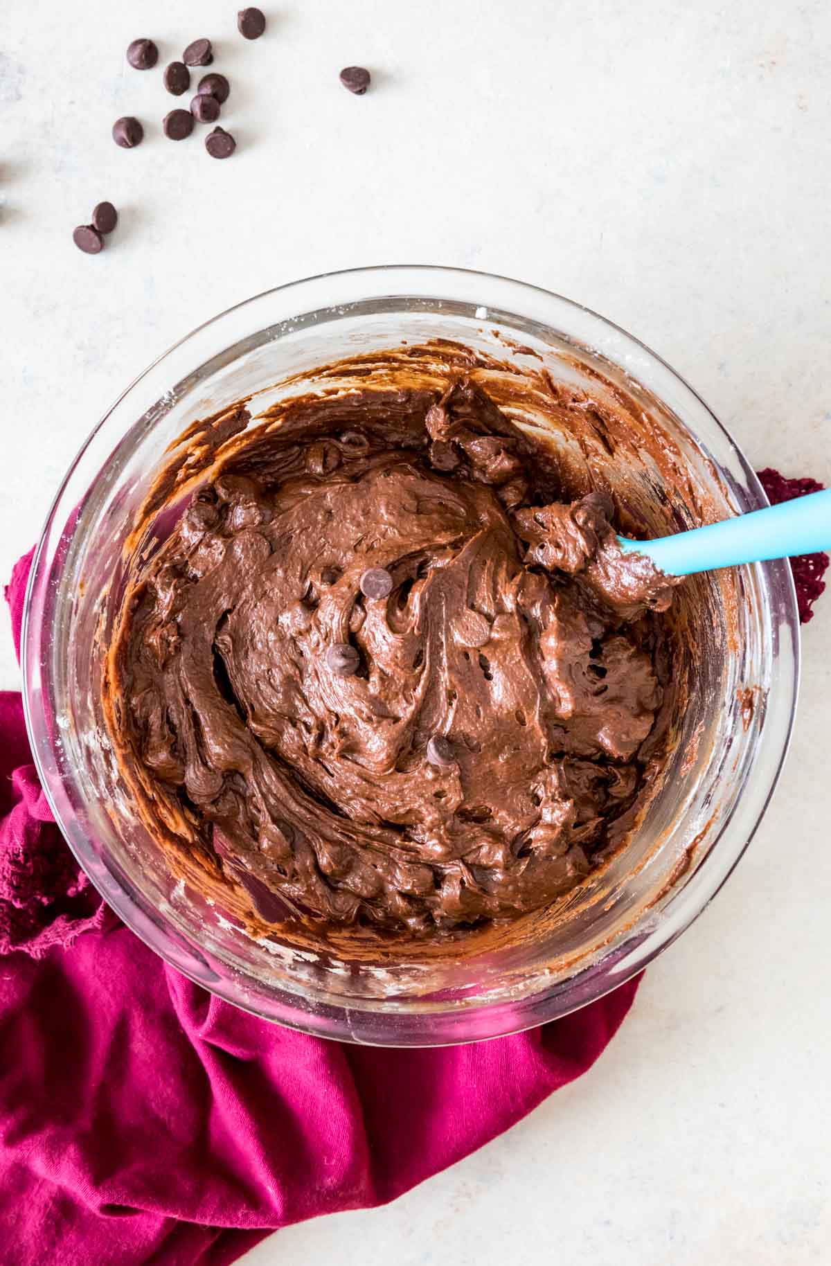 Glass bowl of brownie batter with chocolate chips, sitting on magenta towel