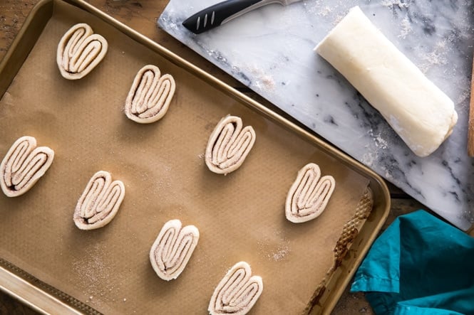 Sliced palmier dough on a cookie sheet, showing how they look before baking and how far to space apart