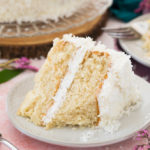 Slice of coconut cake on white plate with bite taken