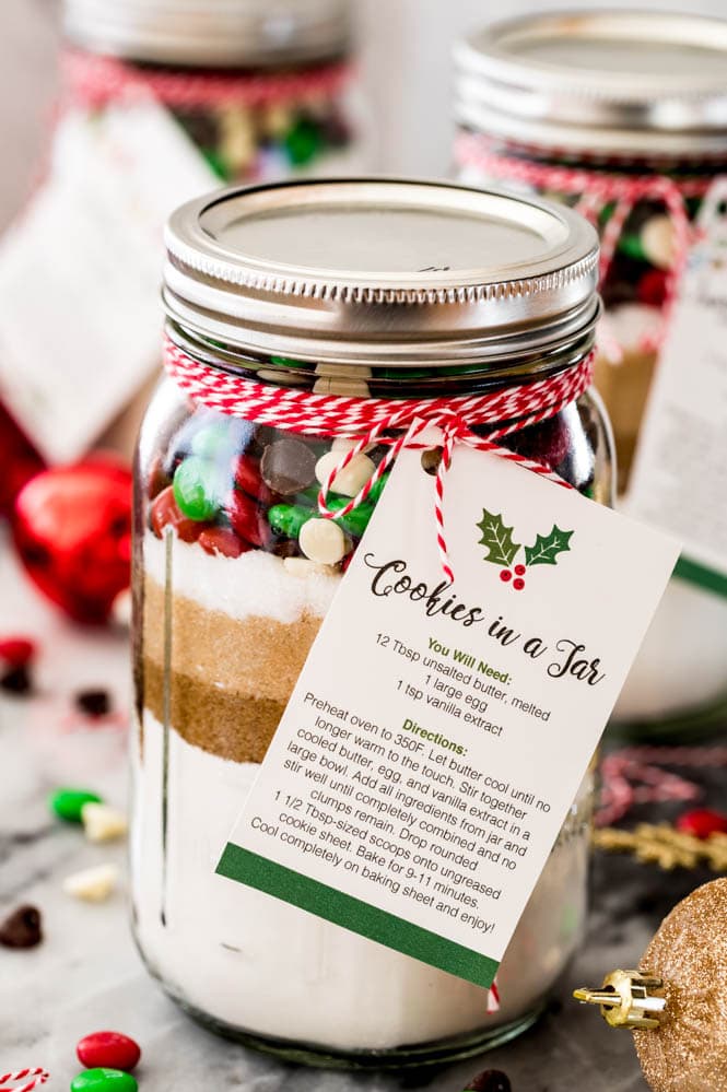 Clear mason jar of cookie mix with pretty layers and holiday colored toppings