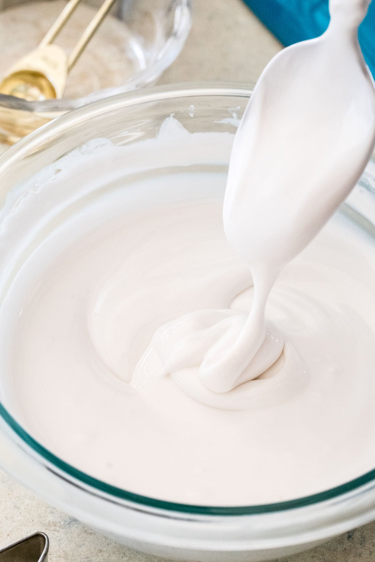 royal icing drizzling off spoon into a glass bowl of icing