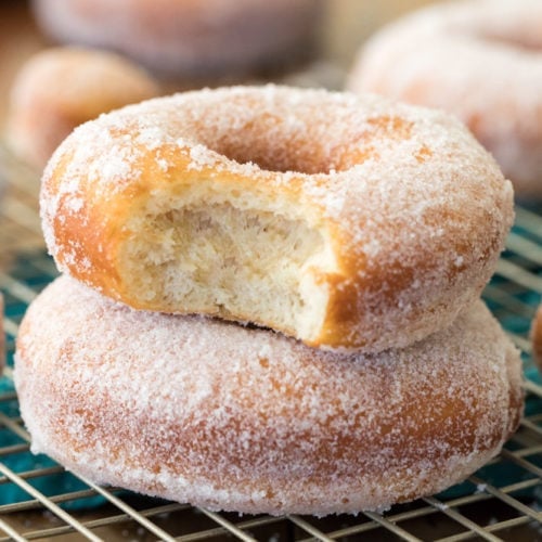 Sugared donuts stacked on top of each other. Top one has bite taken out