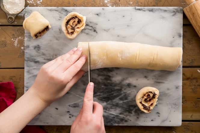 Cutting log of chocolate sweet roll dough on marble