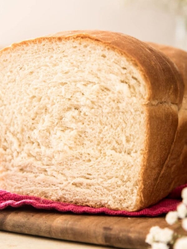 loaf of bread on a red towel on a wooden cutting board with white flowers in foreground and background