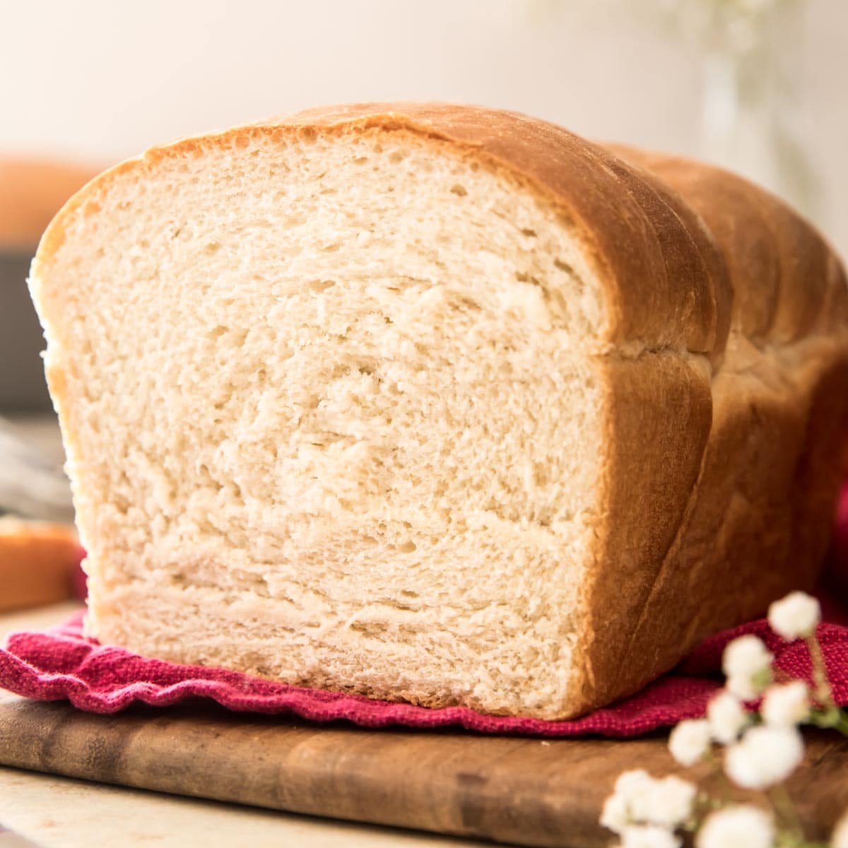 loaf of bread on a red towel on a wooden cutting board with white flowers in foreground and background