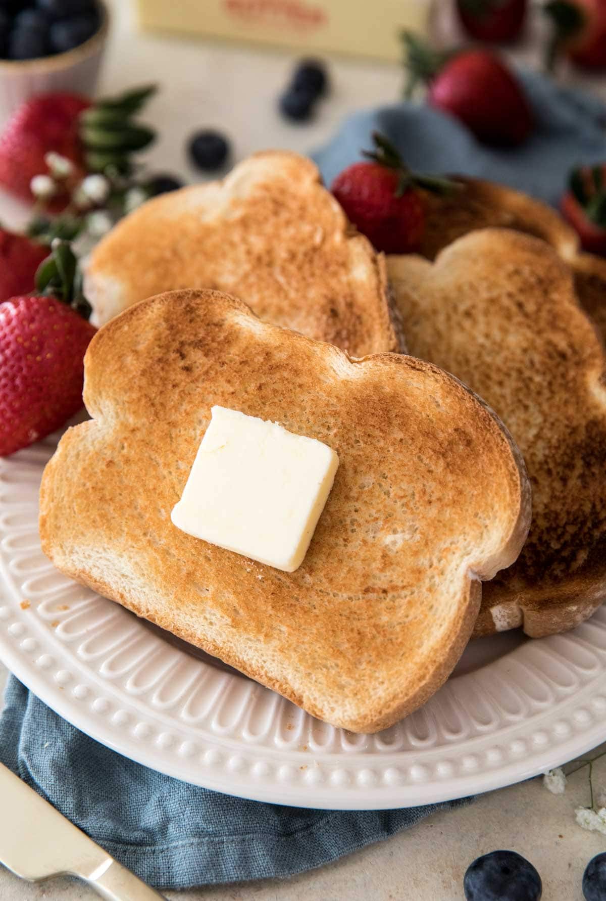 Toast with butter on a white plate surrouned by strawberries