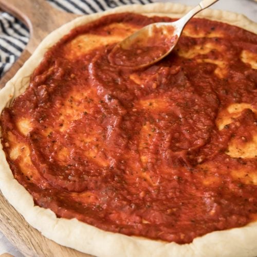 Spreading pizza sauce over pizza dough