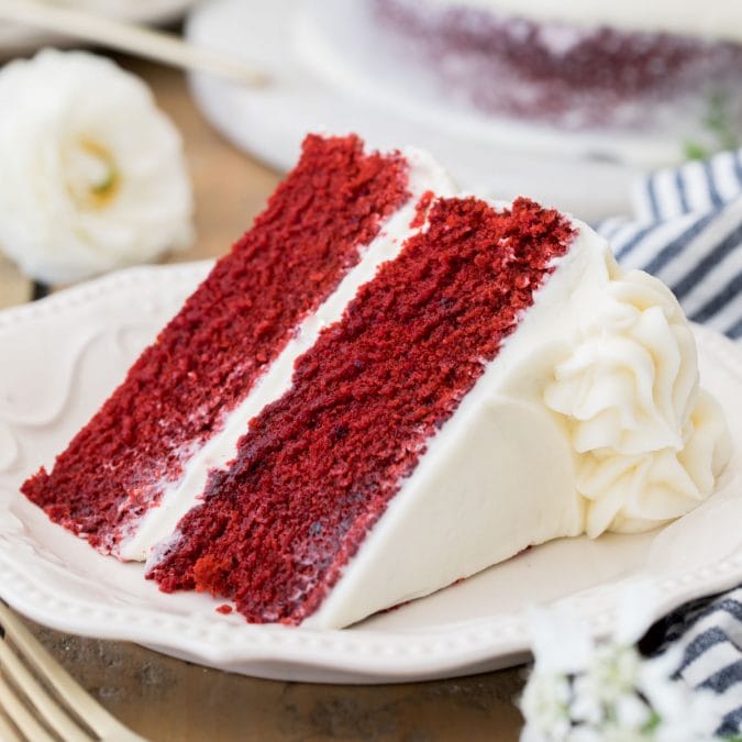 Slice of frosted Red Velvet cake on a white plate