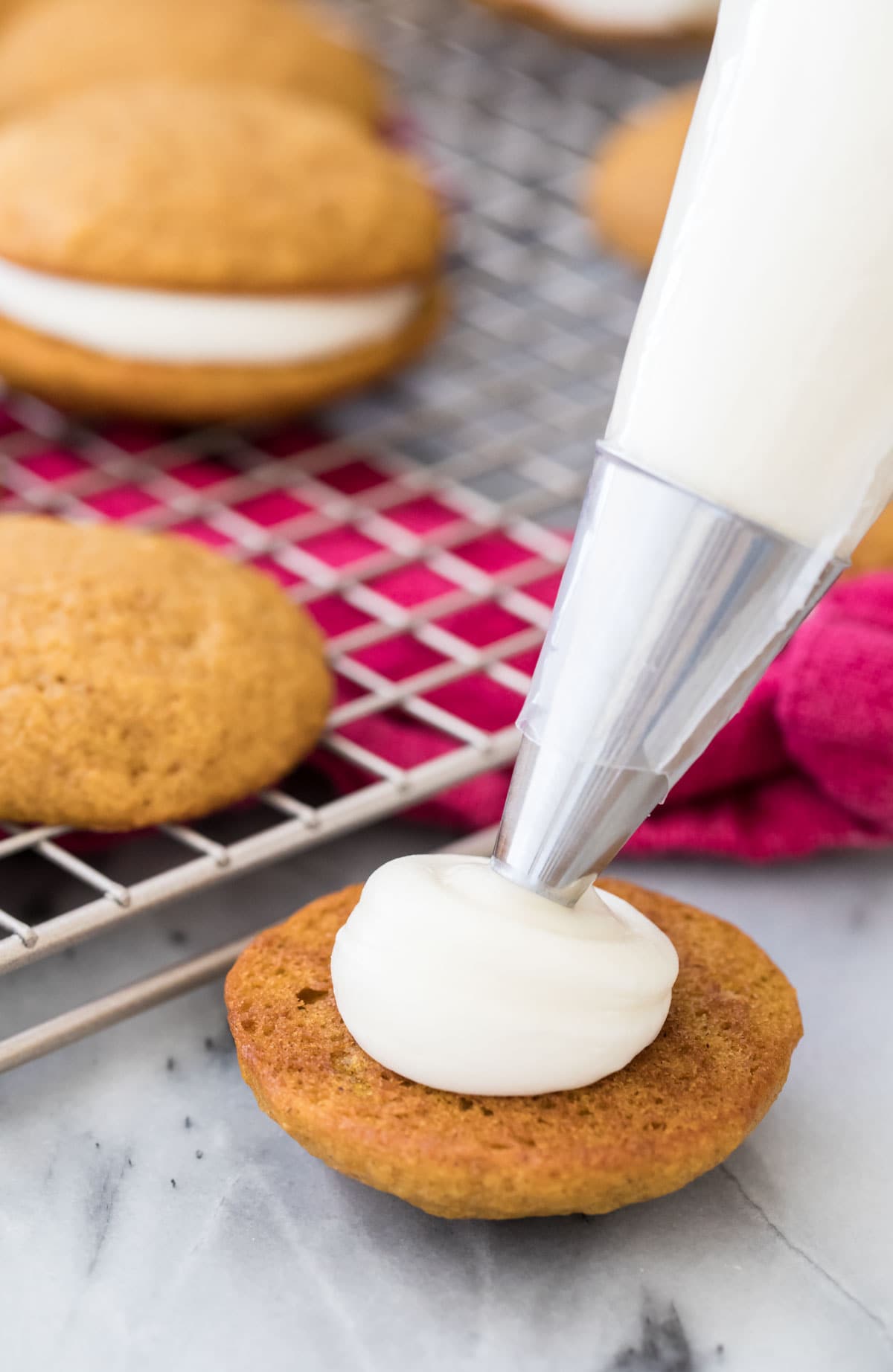 piping cream cheese frosting onto pumpkin cookie
