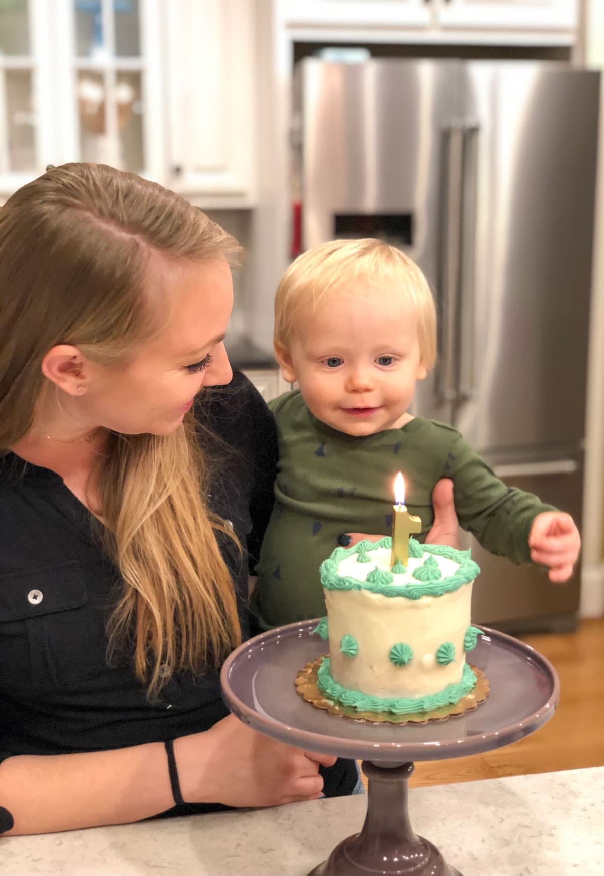 baby boy being held by mom in front of small birthday cake
