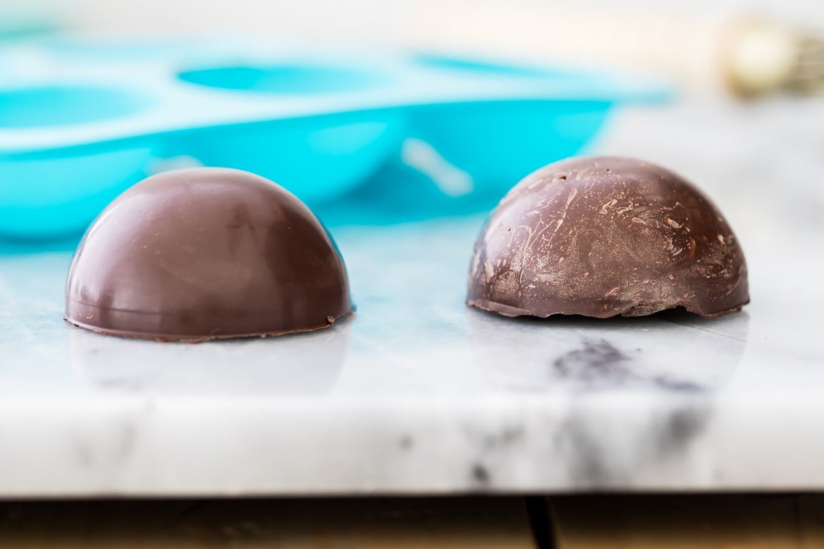 shiny tempered chocolate half sphere on left, chalky, white-streaked un-tempered chocolate half sphere on right