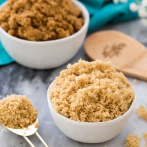 Light brown sugar in a white bowl next to spoonful of light brown sugar