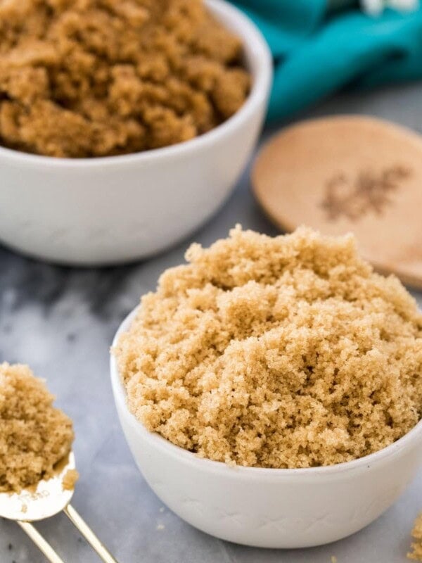 Light brown sugar in a white bowl next to spoonful of light brown sugar