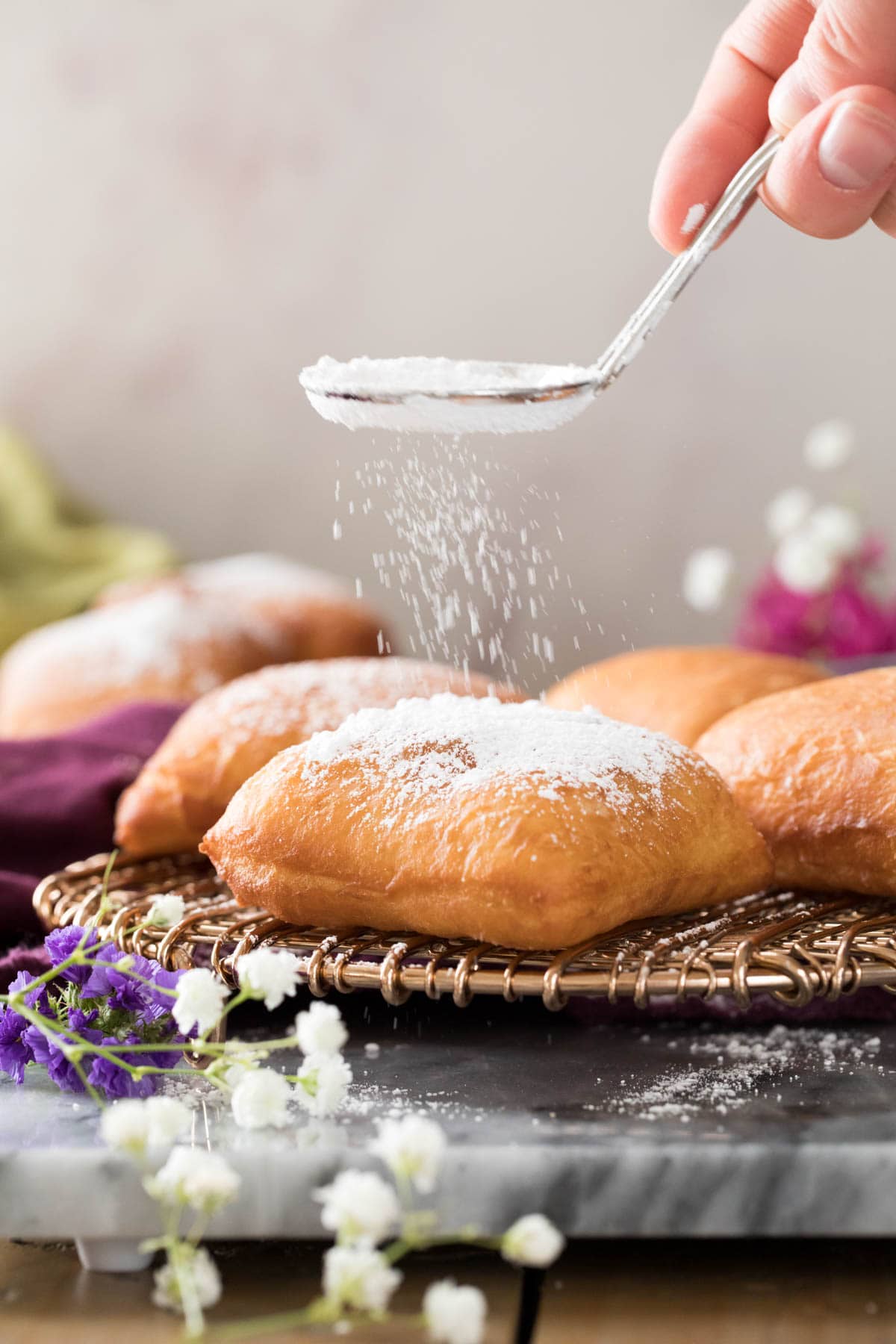 sprinkling powdered sugar over golden brown beignet