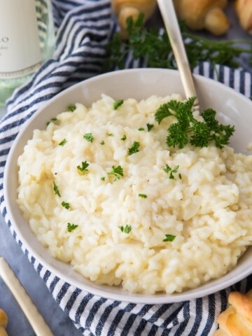 Risotto in a white bowl sprinkled with parsley on top of a blue and white striped kitchen towel