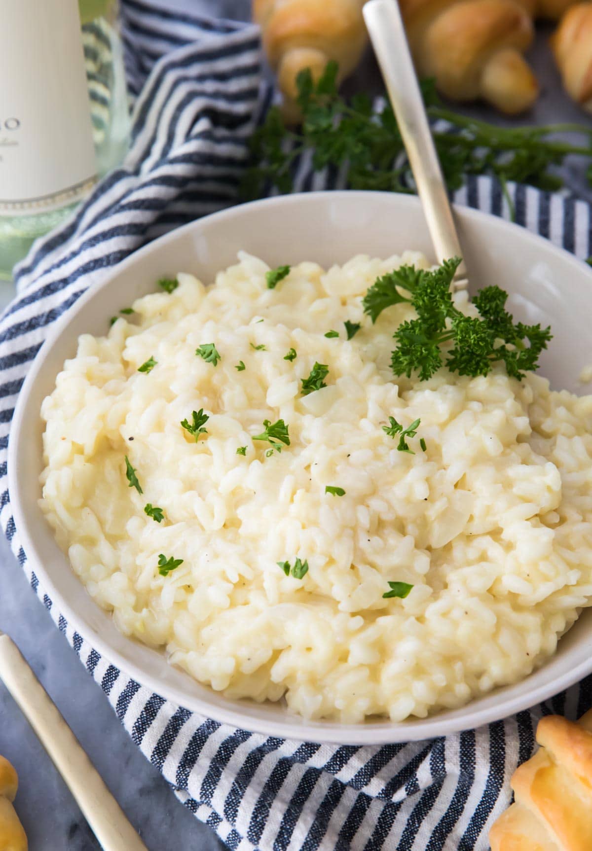 Risotto in a white bowl sprinkled with parsley on top of a blue and white striped kitchen towel