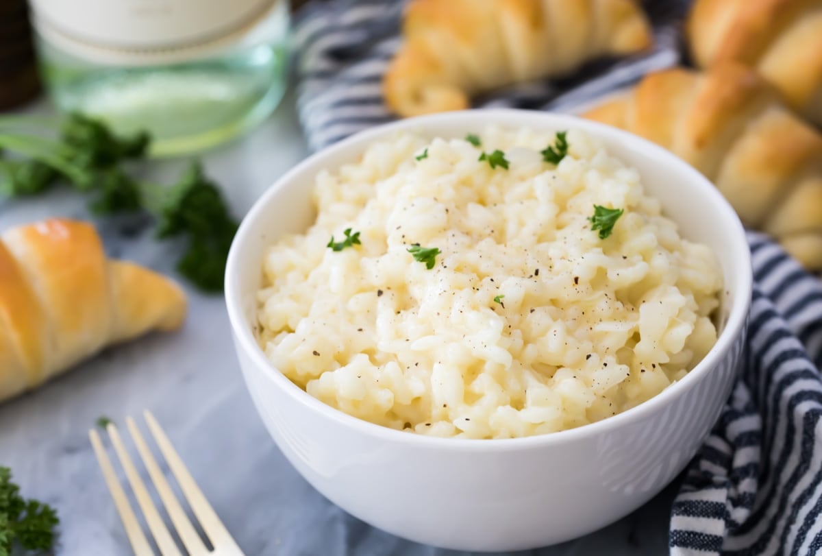 Easy risotto in a white bowl with crescent rolls in the background