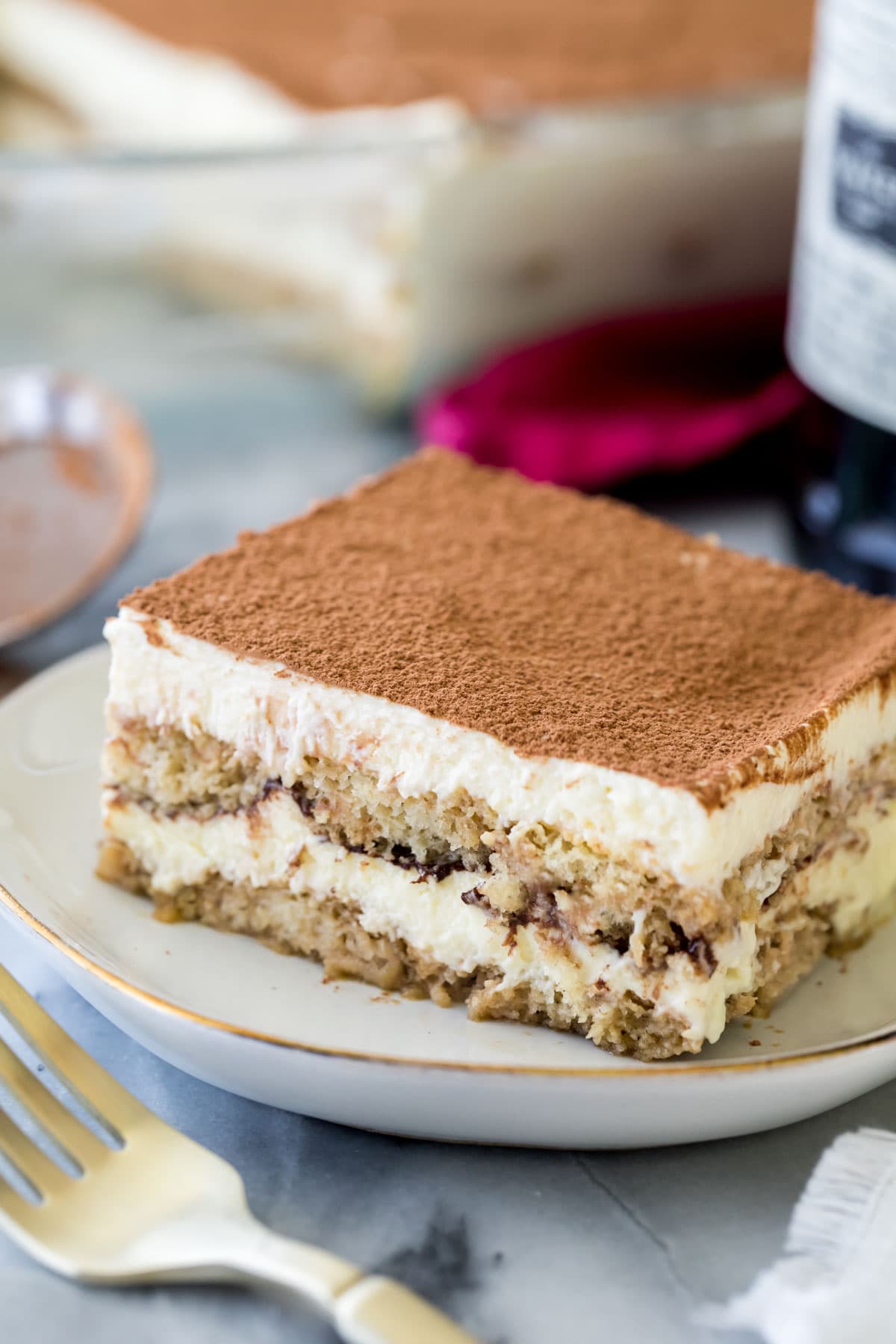 Tiramisu on white plate with gold trim next to a fork