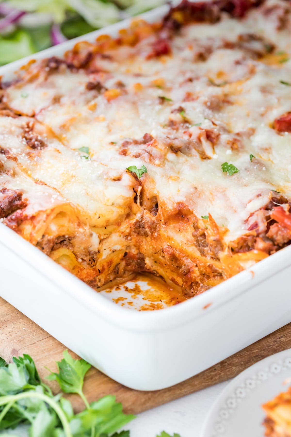 Up close shot of lasagna with a piece cut out in white baking dish