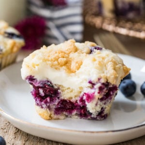 Closeup of blueberry cream cheese muffin with a bite taken out of it on a white plate.