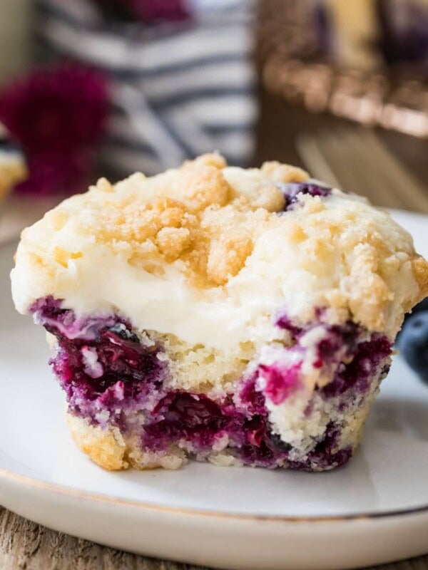Closeup of blueberry cream cheese muffin with a bite taken out of it on a white plate.
