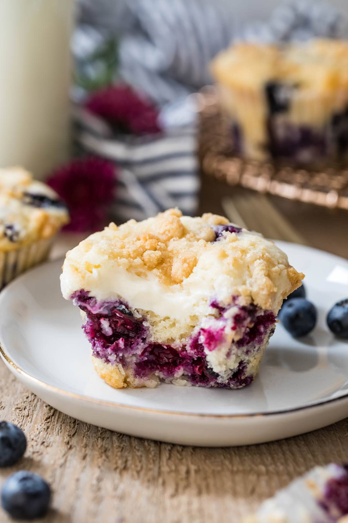 Blueberry muffin with a bite taken out on a white plate next to blueberries.