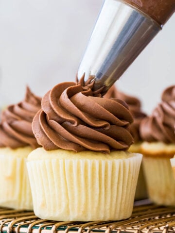 Chocolate frosting being piped onto vanilla cupcakes.