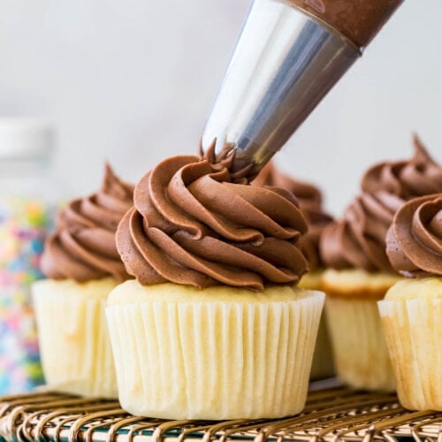 Chocolate frosting being piped onto vanilla cupcakes.