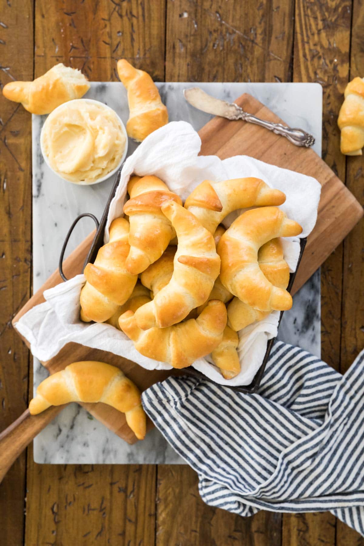 Overhead view of rolls in a square dish lined with a white towel next to a small round dish of butter