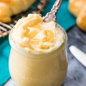 Closeup of honey butter in a clear glass jar with a knife inside.