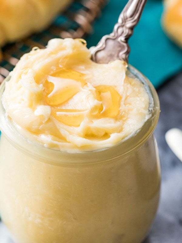 Closeup of honey butter in a clear glass jar with a knife inside.